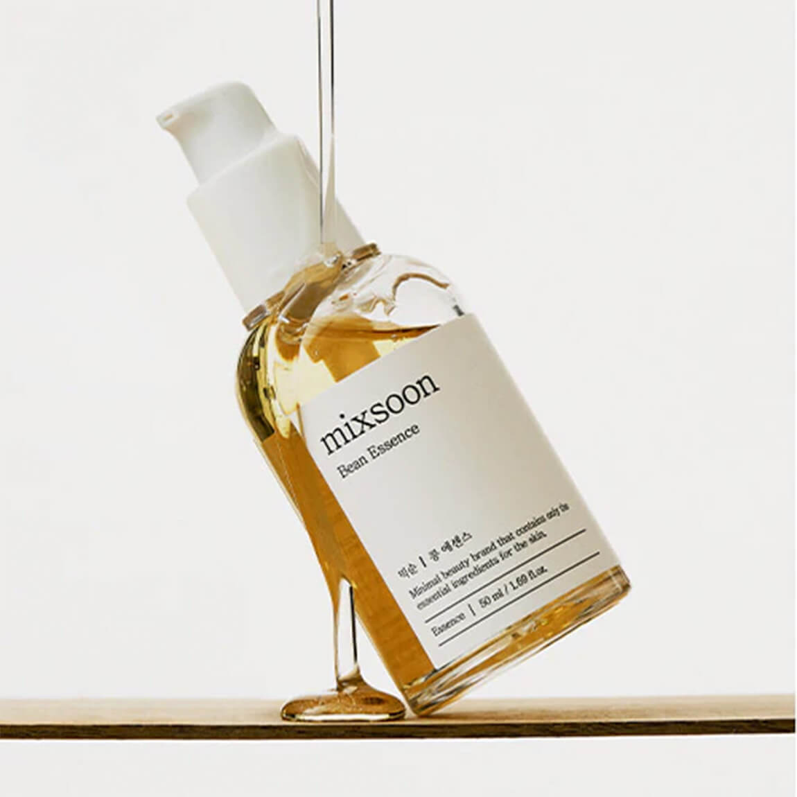 Bottiglia di Mixsoon Bean Essence inclinata con il prodotto che cola, su sfondo neutro. Skincare coreana vegana e cruelty-free con ingredienti fermentati per idratazione e luminosità.